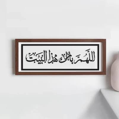 Framed Arabic calligraphy on a white wall with a vase on the side.