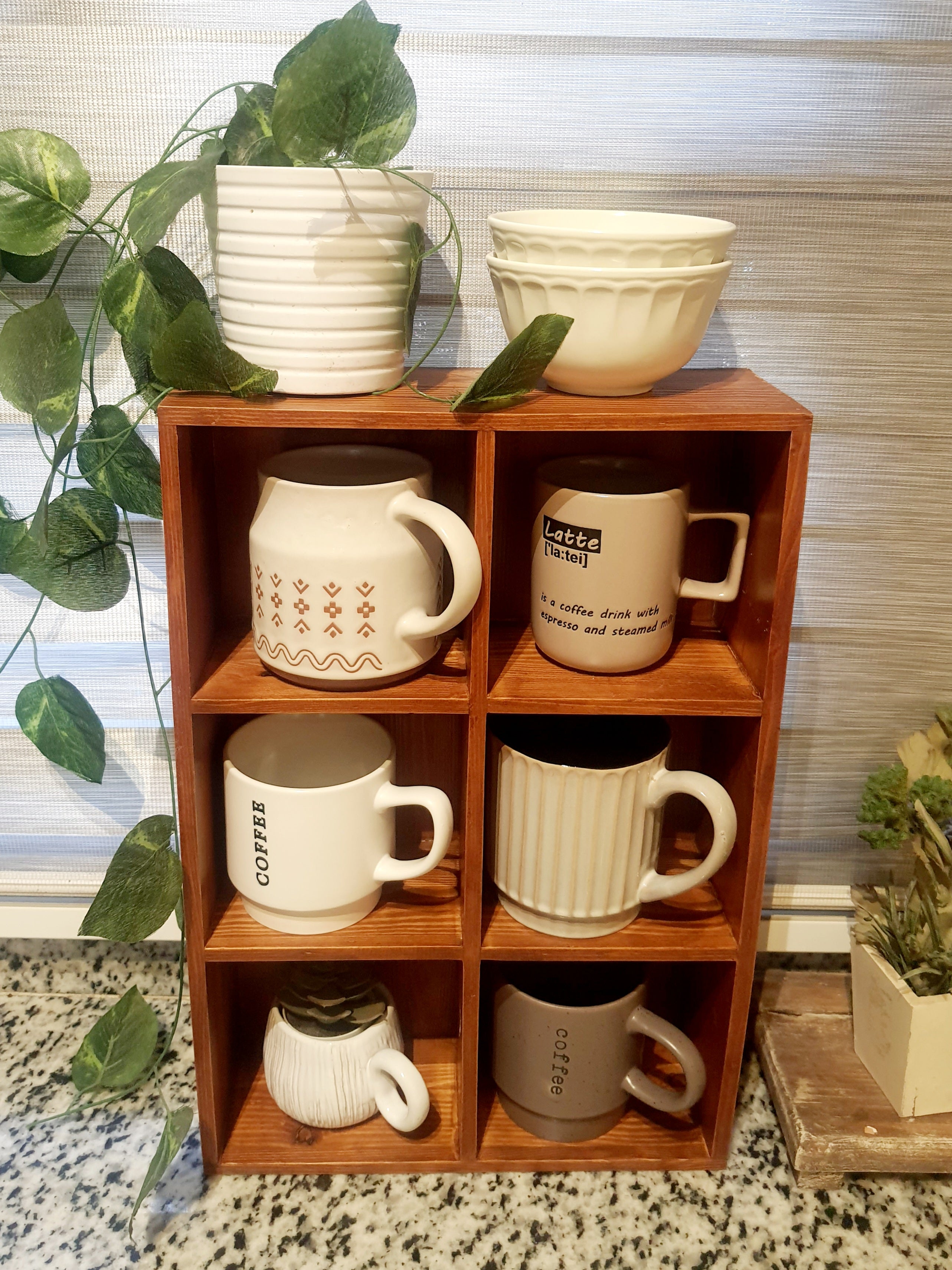 Wooden shelf with six mugs and two plants on a patterned surface