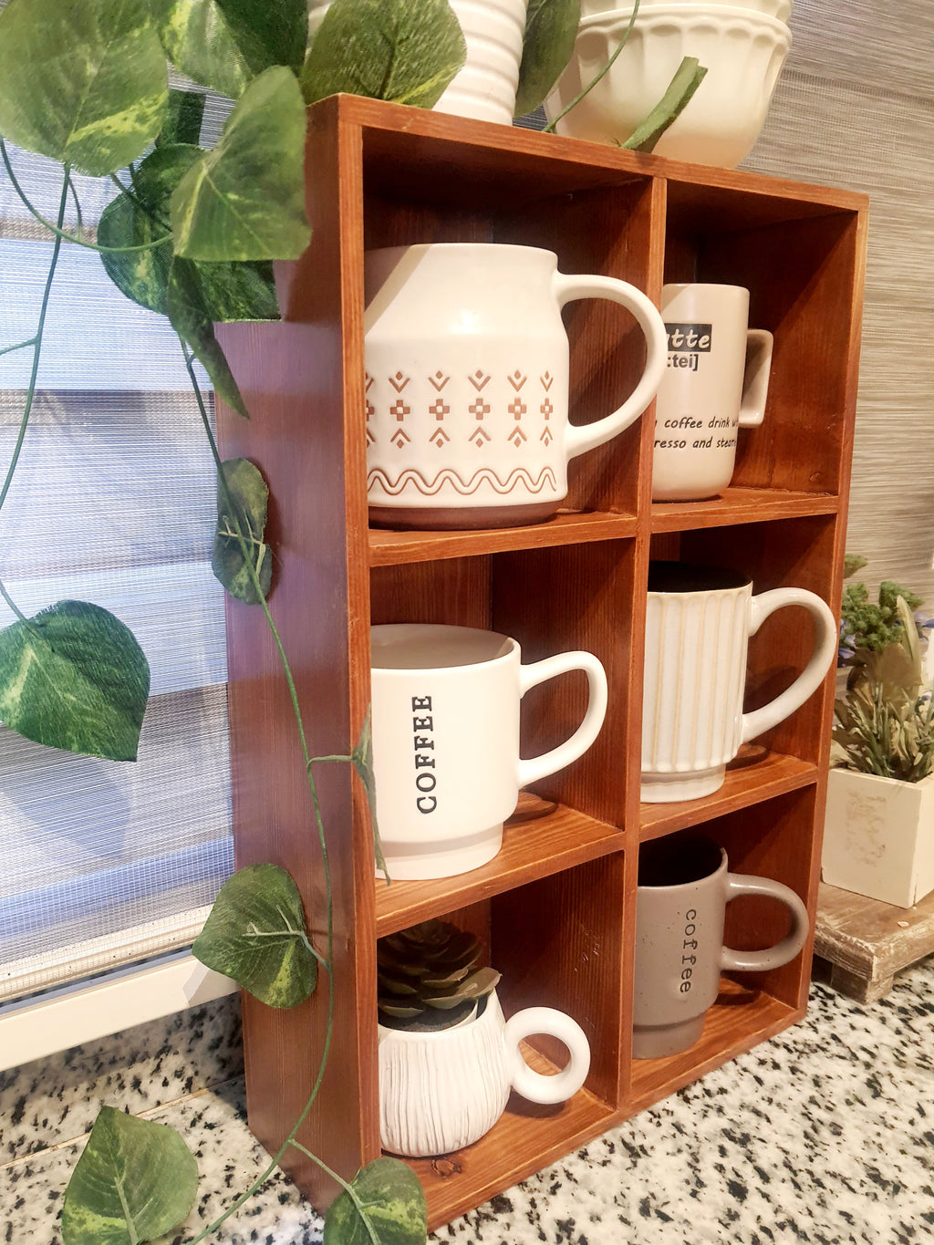 Wooden shelf with various mugs and a plant in the background