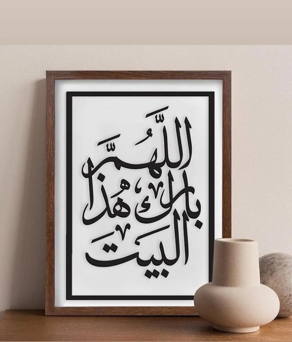 Framed Arabic calligraphy print on a wall with a vase and rock in the foreground.