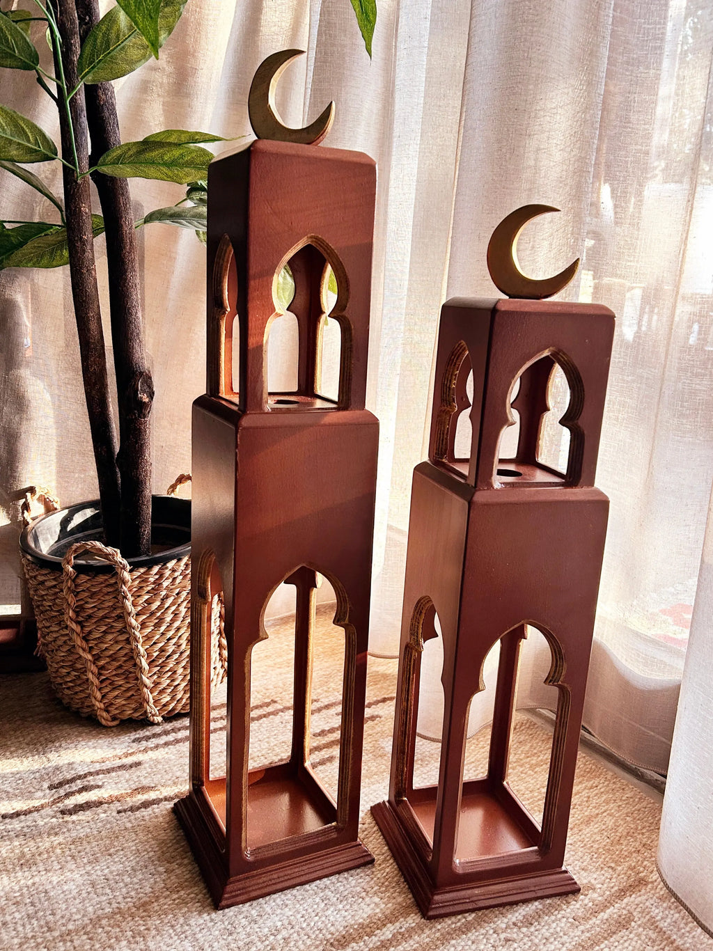Two wooden lanterns with crescent moon designs on top, placed indoors.
