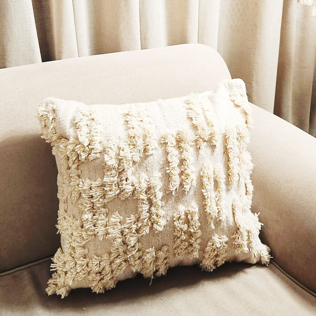 Textured beige pillow on a beige sofa with light curtains in the background