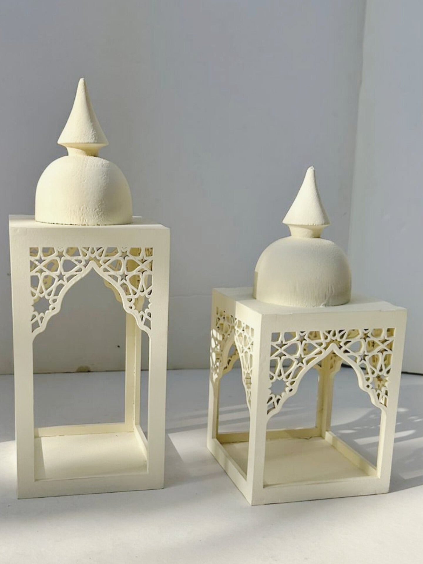 Two cream-colored lanterns with intricate cut-out designs on a light gray background