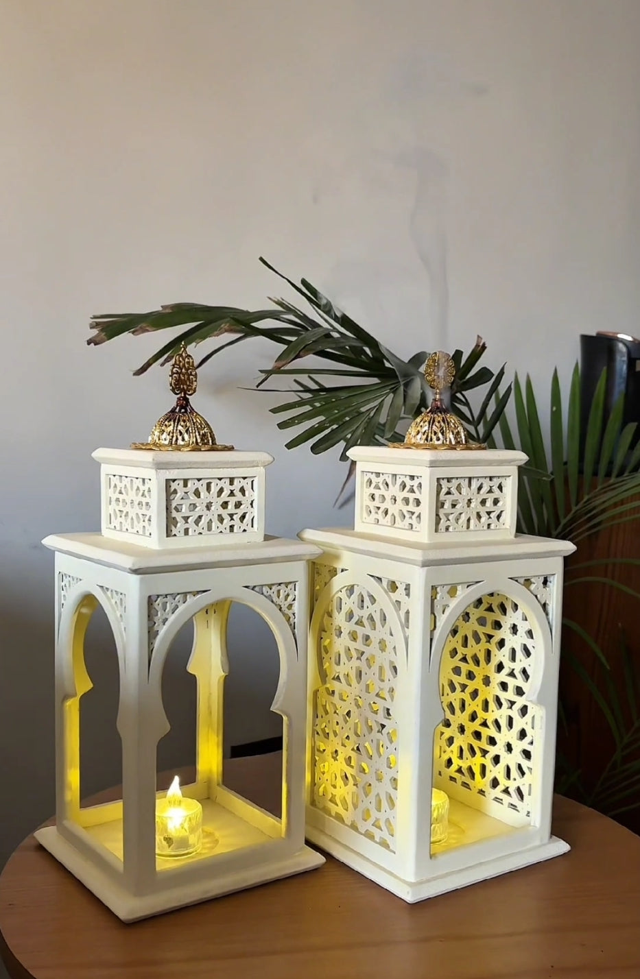 Two white decorative lanterns with intricate patterns on a wooden surface.