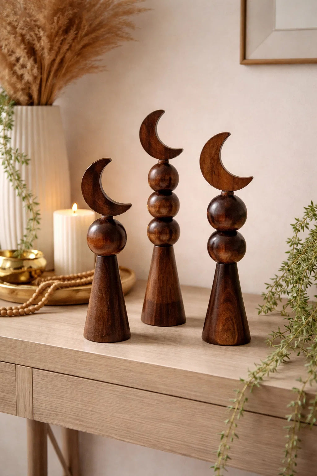 Wooden decorative items shaped like crescent moons on a wooden surface with plants and candles in the background.