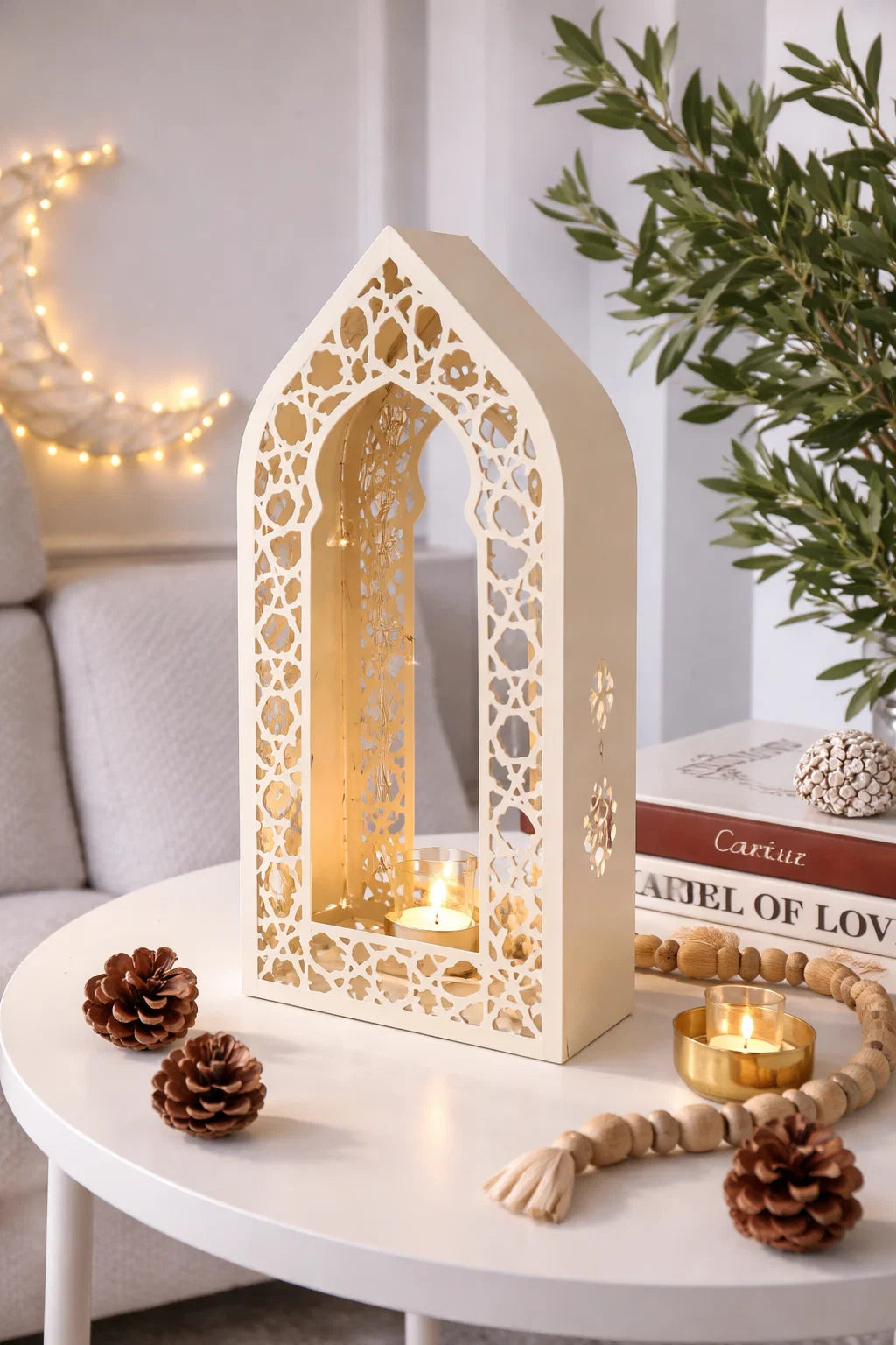 Decorative lantern with intricate cut-out design on a table with candles and pinecones.