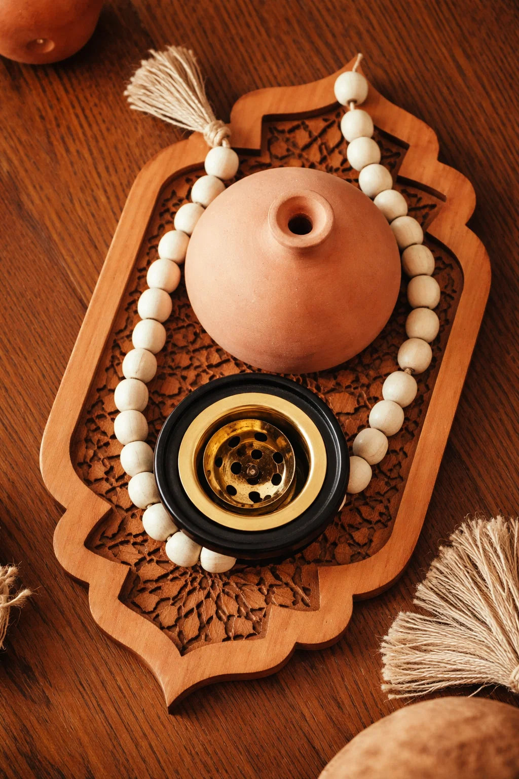 Decorative item with a terracotta pot, beads, and a black metal component on a wooden surface.