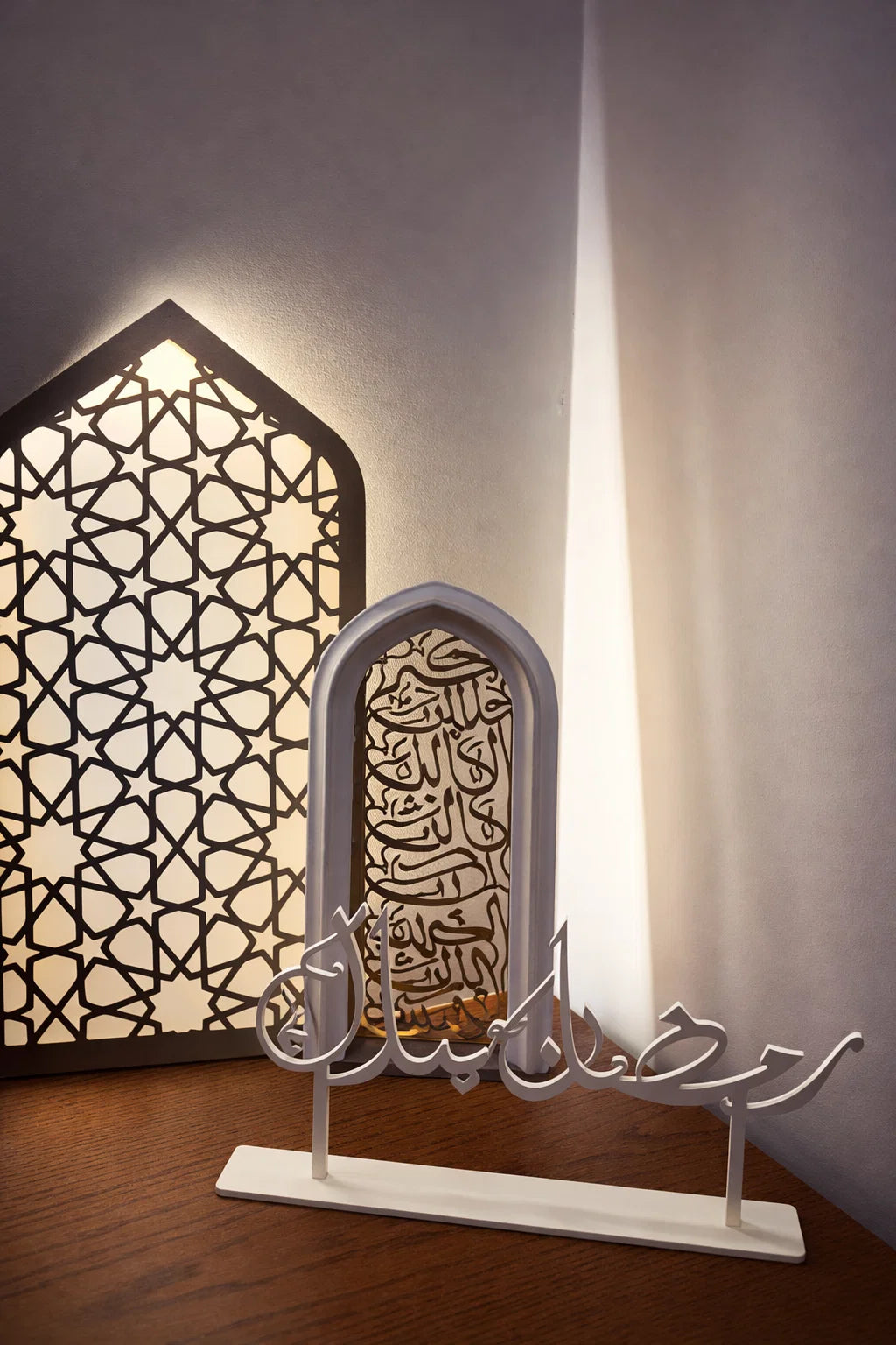 Decorative metal art piece with Arabic calligraphy on a stand, illuminated by a lamp.