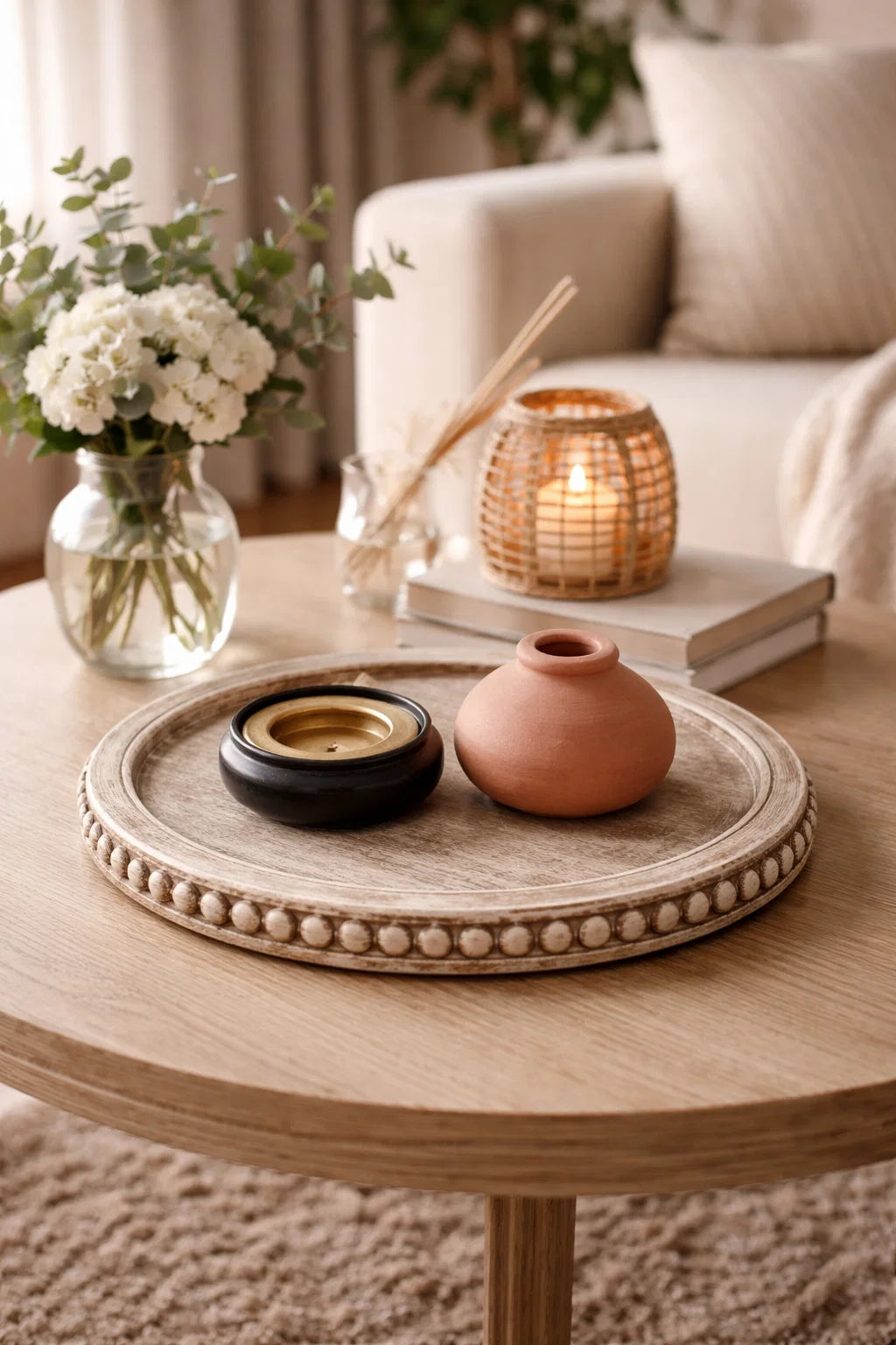 Decorative items on a wooden coffee table with a vase of flowers and a candle in the background.