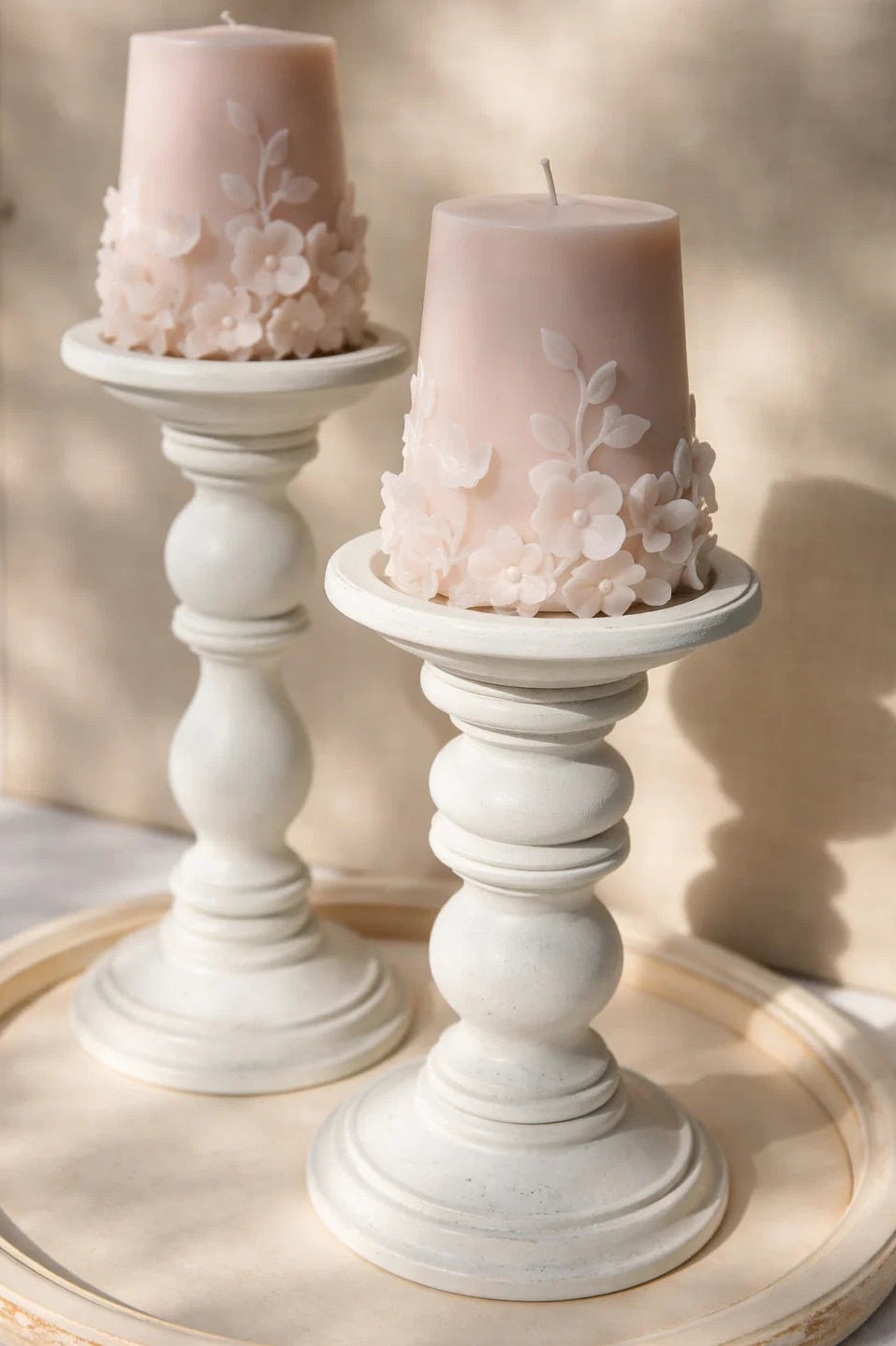 Two pink candles with floral decorations on white candlesticks on a wooden surface.